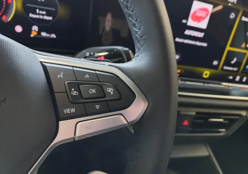 Gros plan sur les commandes au volant du Volkswagen Tiguan 2025, avec affichage numérique en arrière-plan.