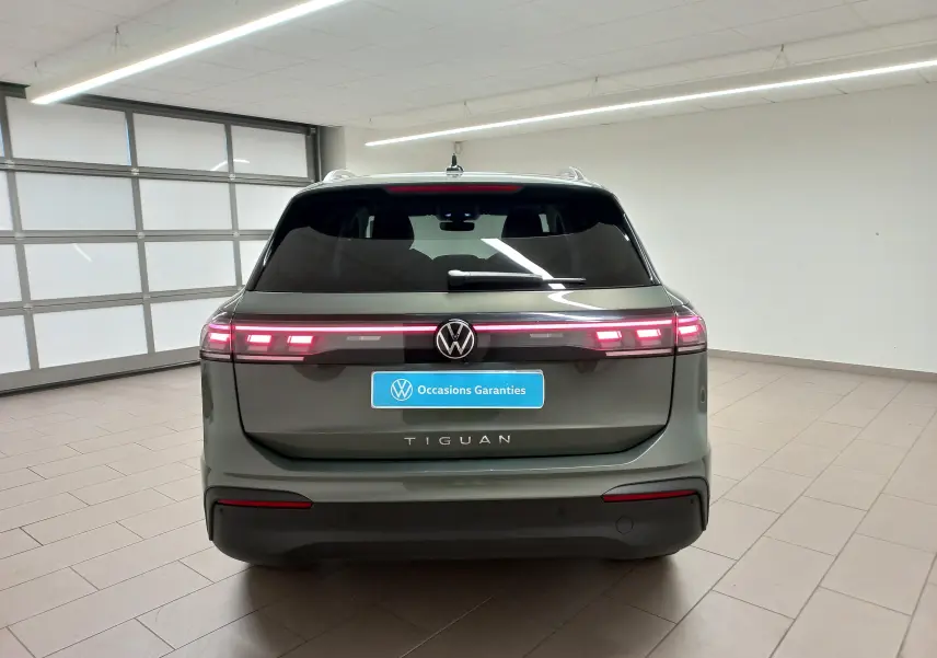 Vue arrière d'un Volkswagen Tiguan 2025 vert Cipressino avec feux LED allumés dans un showroom.
