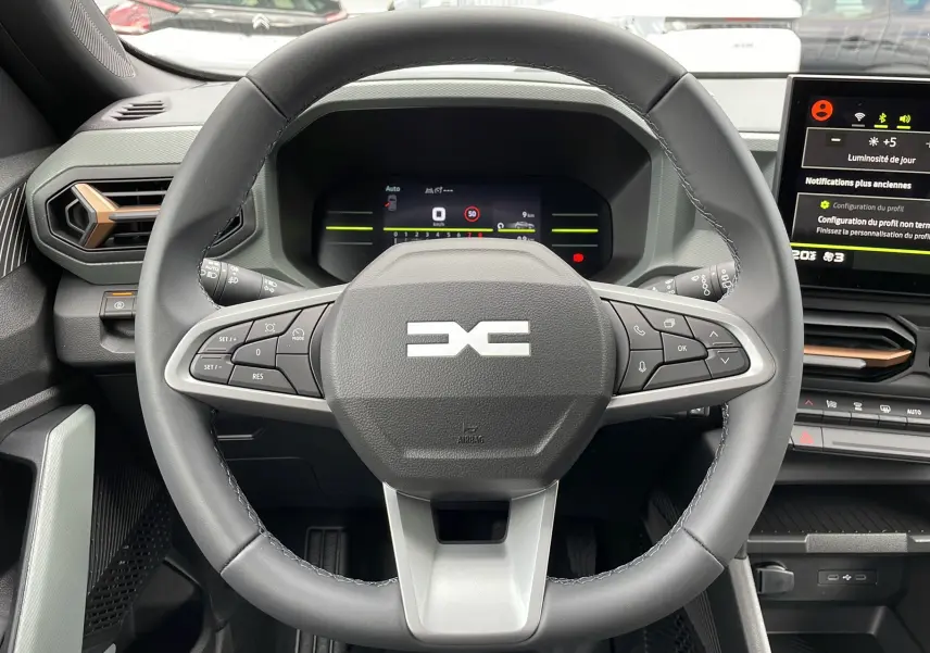 Vue intérieure centrée sur le volant cuir du Dacia Duster 2025, avec tableau de bord numérique et écran tactile visible.