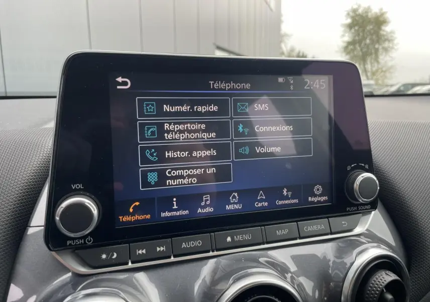 Écran tactile central du Nissan Juke 2024 gris Silver affichant le menu téléphone avec commandes physiques en dessous.