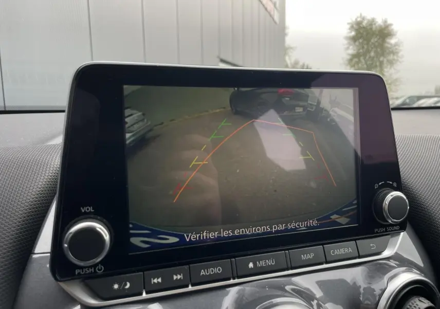 Écran tactile intérieur montrant la caméra de recul du Nissan Juke gris silver, avec les lignes d’aide au stationnement visibles.