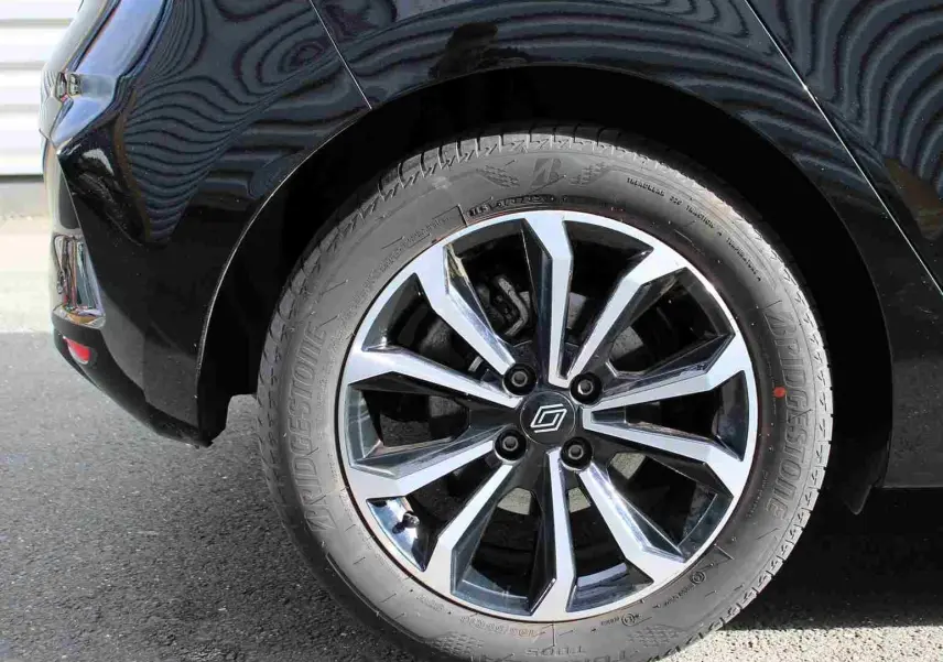 Gros plan sur la roue arrière droite d'une Renault Clio noire étoile métal avec jante alliage bicolore moderne.