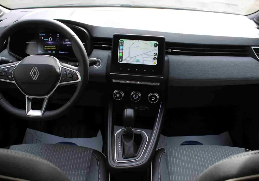 Vue intérieure avant de la Renault Clio 2025 hybride, tableau de bord gris noir avec écran tactile central et volant multifonction.