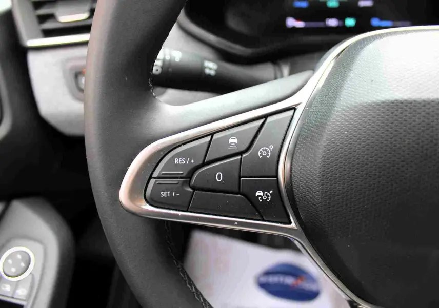 Gros plan sur les commandes de régulateur de vitesse au volant noir de la Renault Clio hybride 2025.