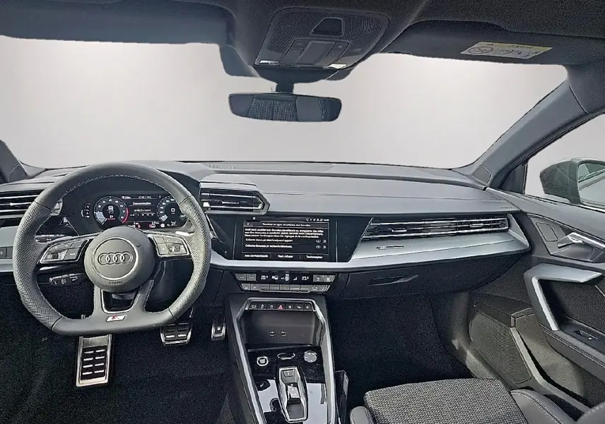 Intérieur Audi A3 Sportback 2026 vu de face, tableau de bord noir avec écran central et volant sport cuir noir.