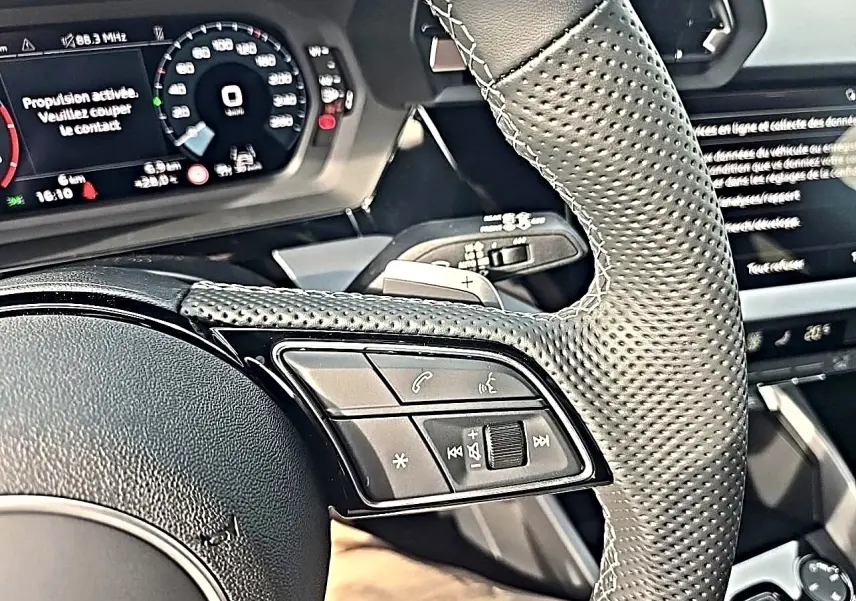 Gros plan sur le volant cuir perforé et les commandes multifonctions à gauche de l'Audi A3 Sportback 2026.
