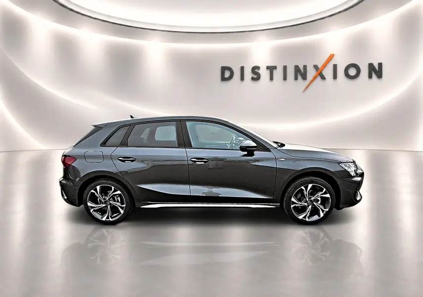Audi A3 Sportback gris Daytona vue de profil côté gauche dans un studio lumineux avec logo Distinxion en arrière-plan.