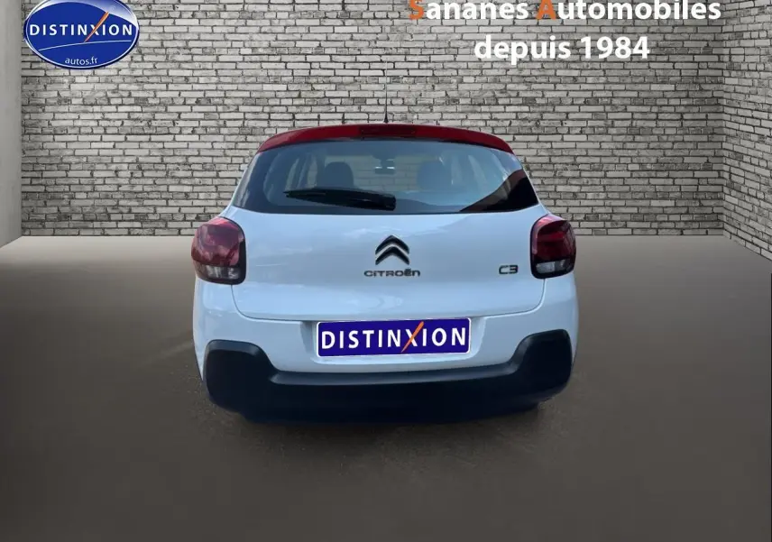 Vue arrière d'une Citroën C3 2023 blanche avec toit rouge et logo distinctif sur fond urbain en briques.