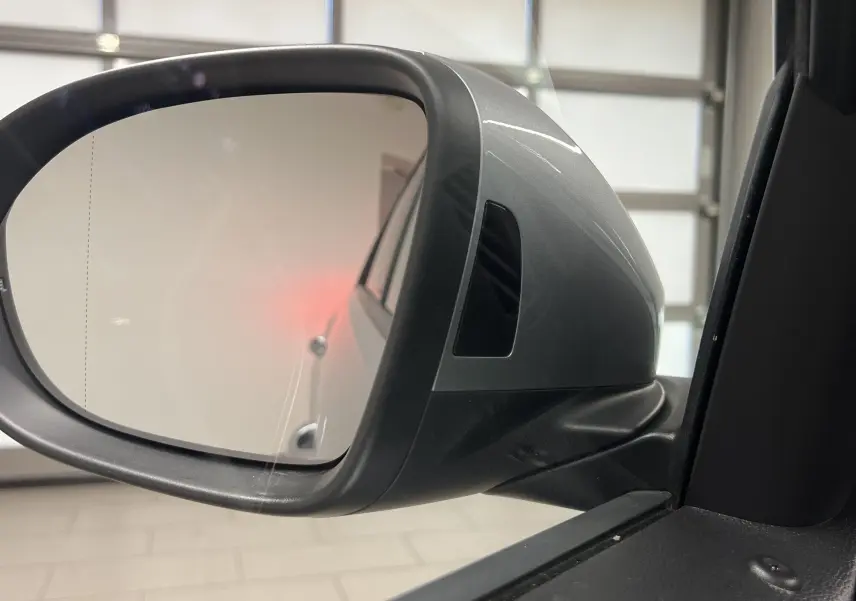 Rétroviseur côté gauche du Volkswagen T-Roc gris pyrite 2024 avec clignotant intégré et carrosserie visible en reflet.