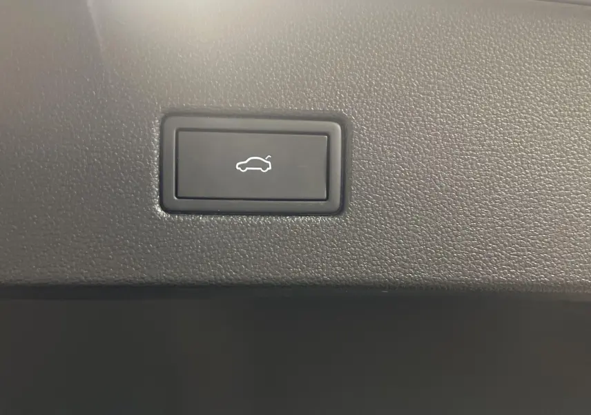 Bouton d'ouverture électrique du coffre sur la garniture intérieure d'un Volkswagen T-Roc 1.5 TSI R-Line 2024 gris Pyrite.