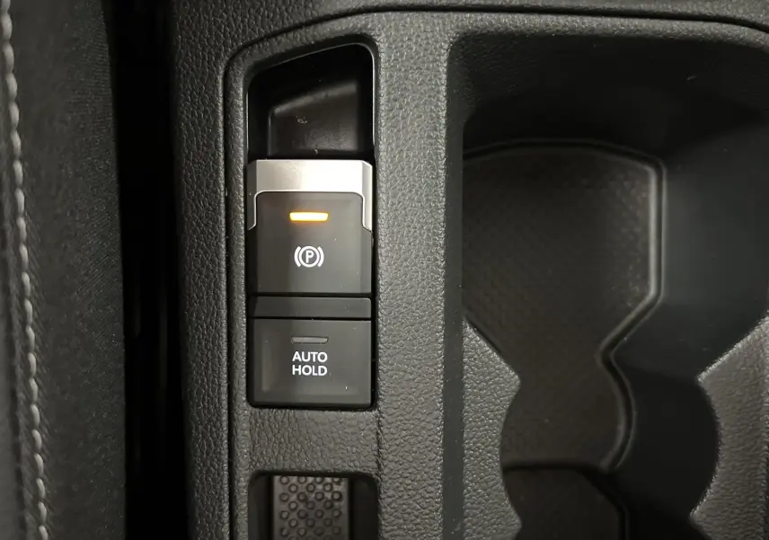 Gros plan sur les commandes de frein à main électrique et auto hold dans l'habitacle du Volkswagen T-Roc gris Pyrite 2024.