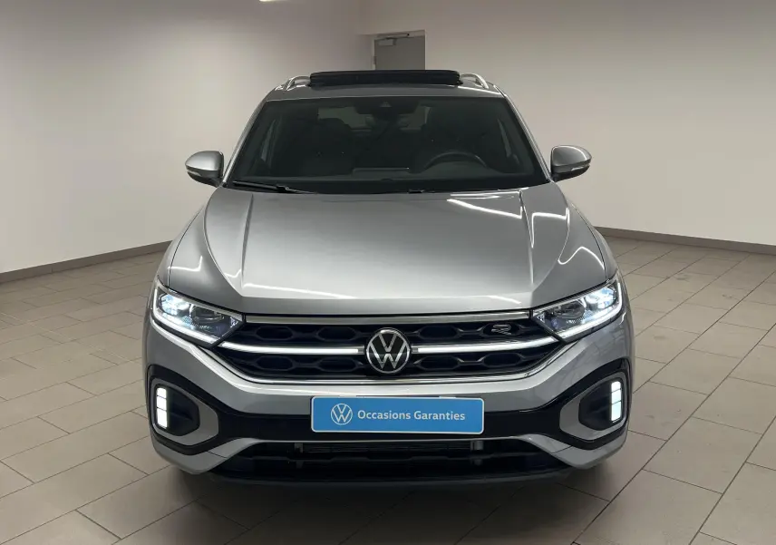 Volkswagen T-Roc gris pyrite vu de face, avec phares Matrix LED allumés et toit ouvrant panoramique visible.