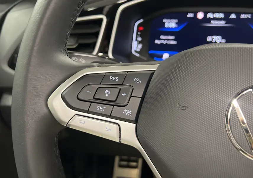 Gros plan sur le volant noir du Volkswagen T-Roc 2024 avec commandes intégrées et tableau de bord numérique bleu.