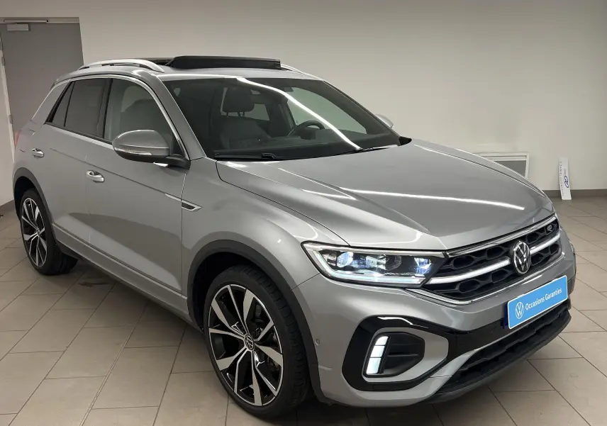 Volkswagen T-Roc gris pyrite en 3/4 avant droit avec jantes 19 pouces et toit ouvrant panoramique visible.