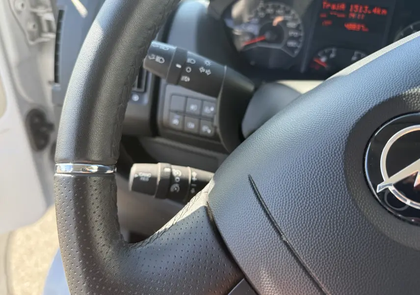 Gros plan sur le volant noir perforé et le tableau de bord digital du fourgon blanc Opel Movano 2.2 BlueHDi 140 L3H2 2023.