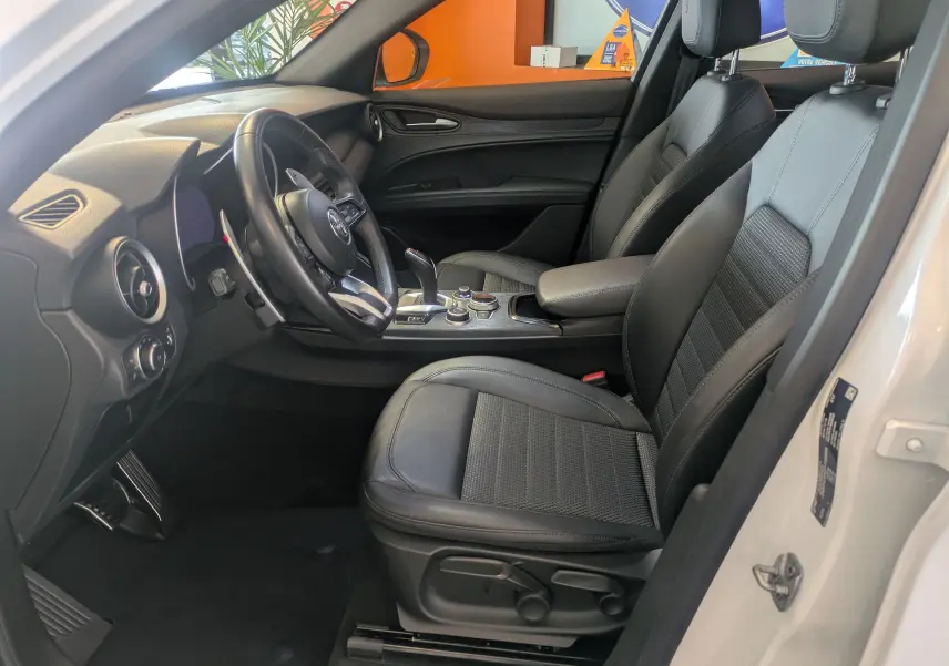 Intérieur de l'Alfa Romeo Stelvio blanc 2023, vue côté conducteur, sièges cuir noir et console centrale moderne.