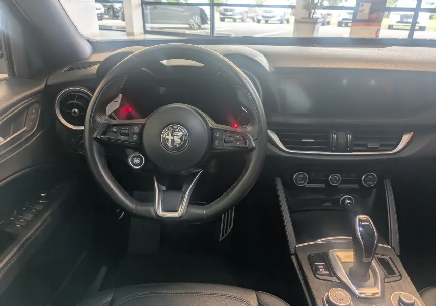 Vue intérieure centrée sur le volant cuir noir et la console centrale d'une Alfa Romeo Stelvio blanche 2023.