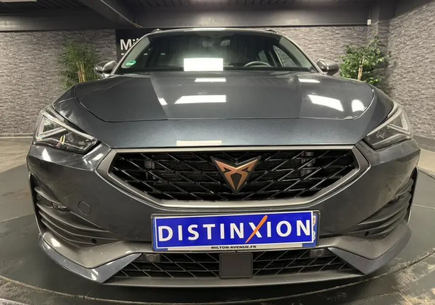 Vue frontale d'une CUPRA Leon Sportstourer gris magnétique avec calandre noire et logo cuivre distinctif.