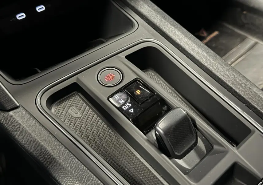 Gros plan sur la console centrale noire du CUPRA Leon Sportstourer 2024 avec levier de boîte auto et bouton start/stop rouge.