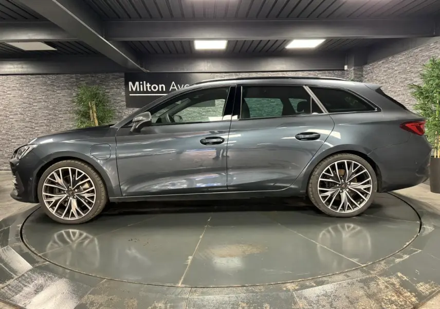 Profil droit d'une CUPRA Leon Sportstourer 1.4 e-Hybrid 245 gris magnétique avec jantes alliage 19 pouces dans un showroom.