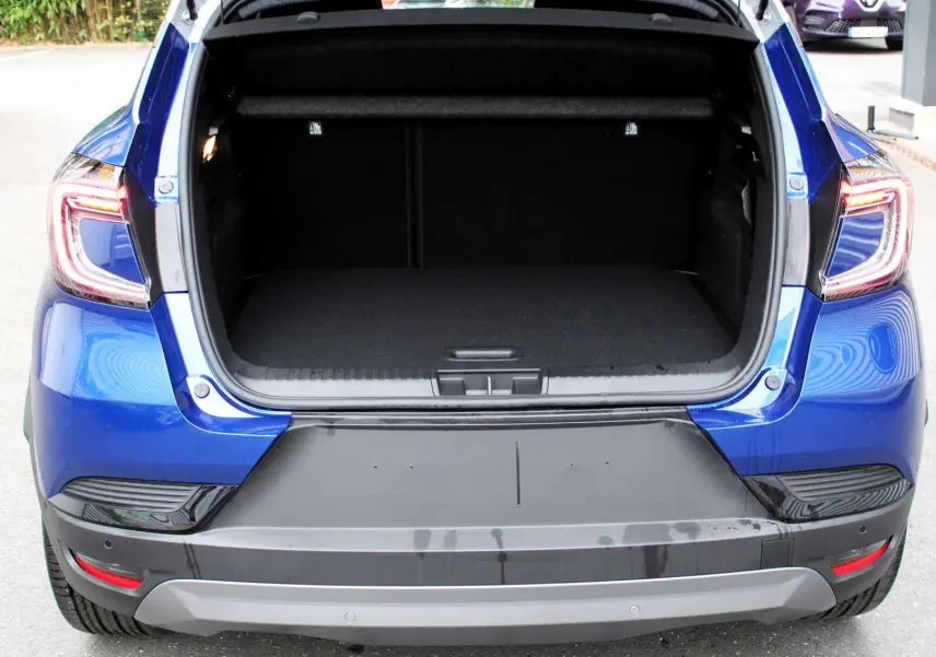 Coffre ouvert vu de l'arrière d'un Renault Captur bleu Iron Metal avec toit gris, feux arrière allumés.