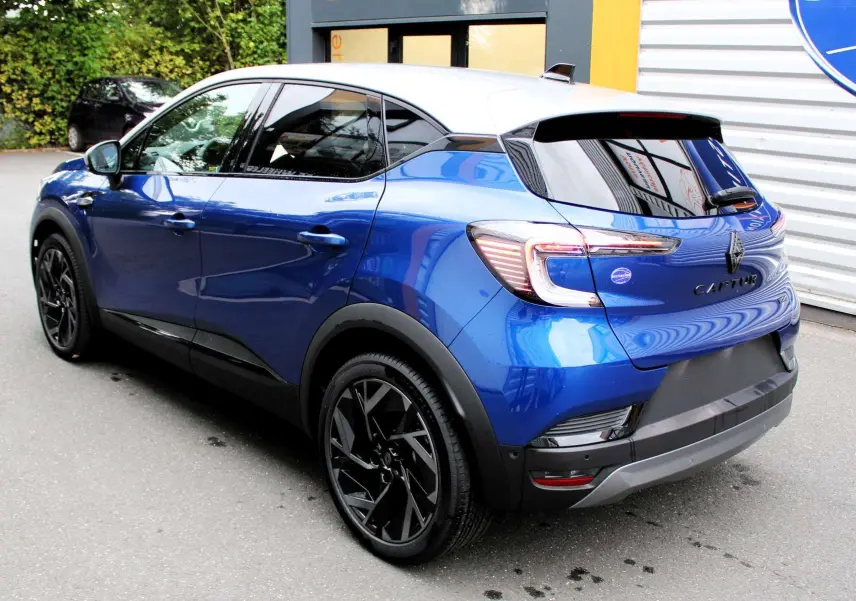 Renault Captur 2025 bleu Iron Metal avec toit gris, vue 3/4 arrière côté gauche, jantes noires distinctives.