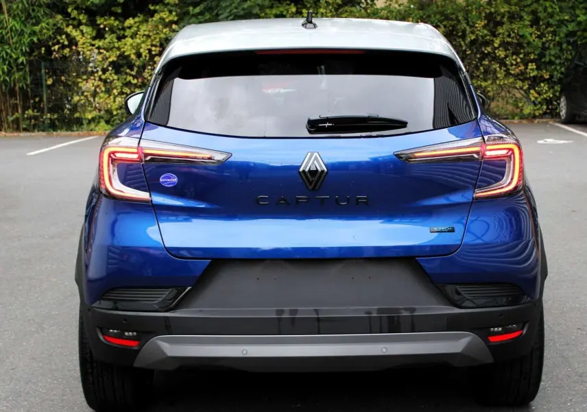 Vue arrière d'un Renault Captur bleu Iron Metal avec toit gris, feux LED allumés et logo central bien visible.