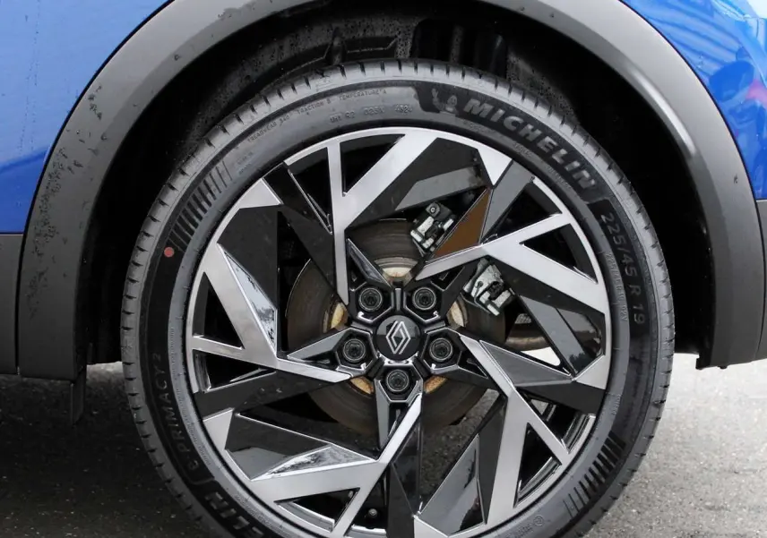 Gros plan sur la roue avant droite du Renault Captur bleu iron metal avec jante alliage noire et argentée au design géométrique.