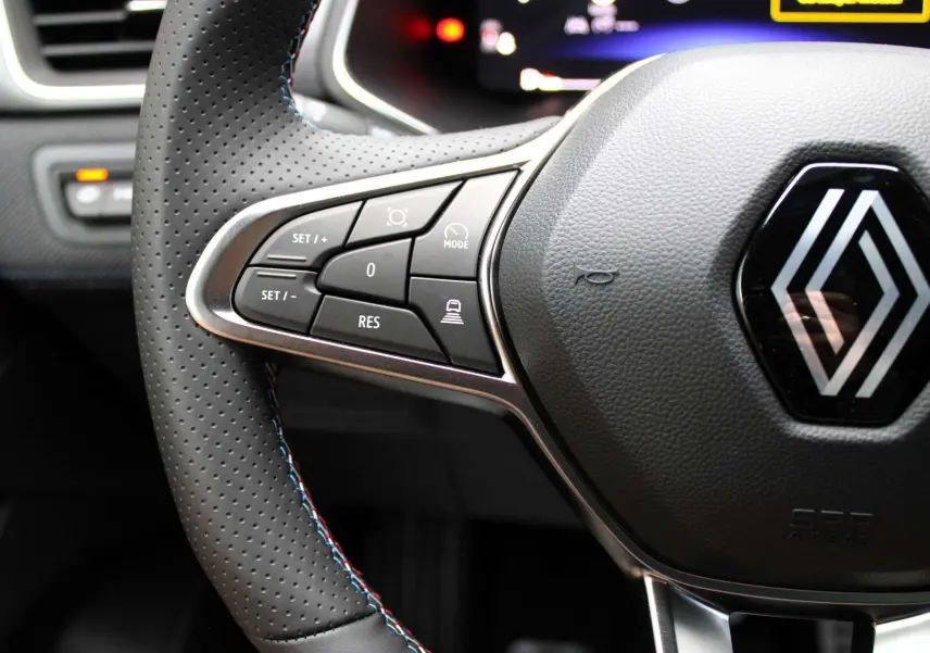 Gros plan sur le volant en cuir perforé avec commandes intégrées et logo Renault au centre du Renault Captur 2025.