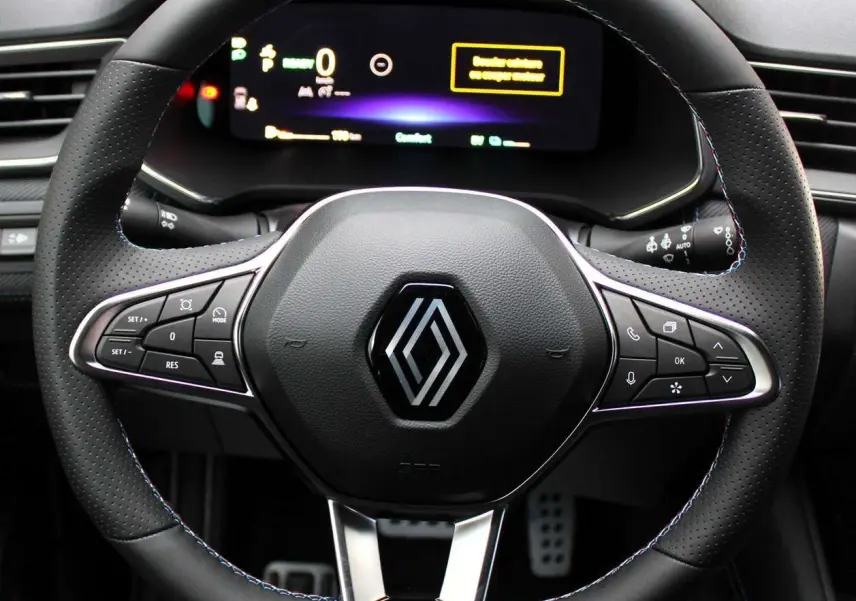 Gros plan sur le volant en cuir noir avec surpiqûres bleues du Renault Captur hybride, tableau de bord digital en arrière-plan.