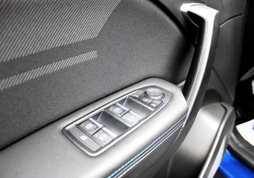 Gros plan sur la commande des vitres côté gauche de la porte d'un Renault Captur 2025 bleu iron metal avec surpiqûres bleues.