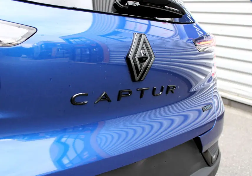 Gros plan arrière droit sur le logo Renault et le nom Captur bleu iron metal avec toit gris du SUV hybride 2025