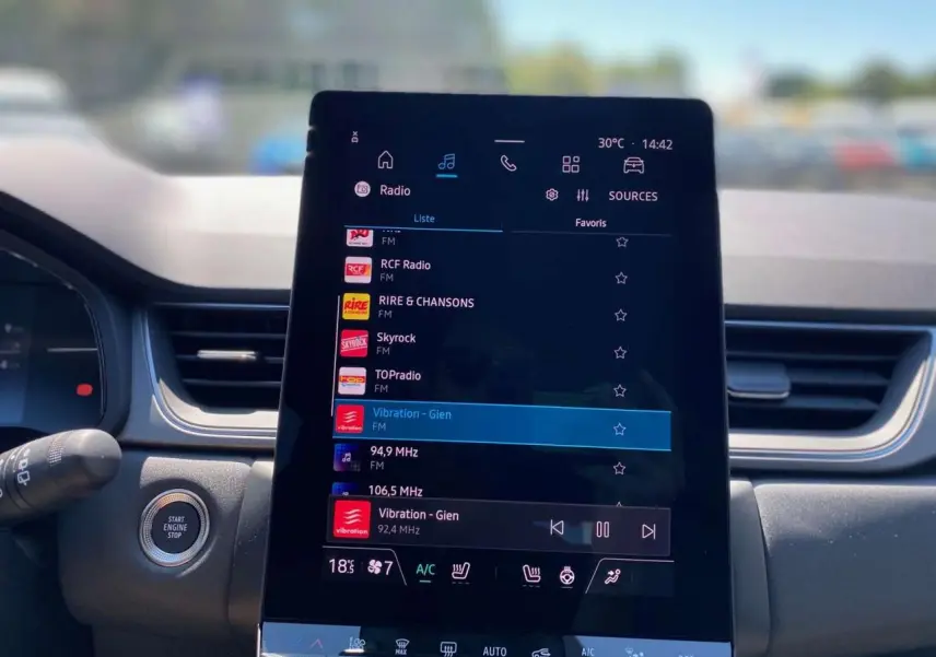 Écran tactile central allumé affichant la radio dans l’habitacle du Renault Captur gris Cassiopée toit noir.