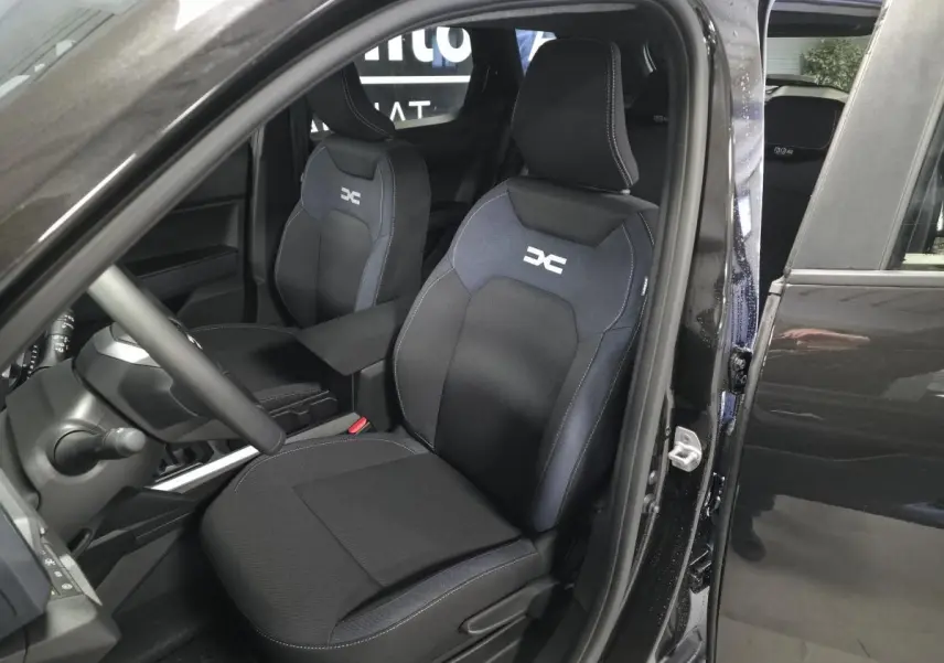 Vue intérieure côté conducteur du Dacia Duster 1.6 Hybrid noir nacré, sièges tissu Denim avec logo DC brodé.