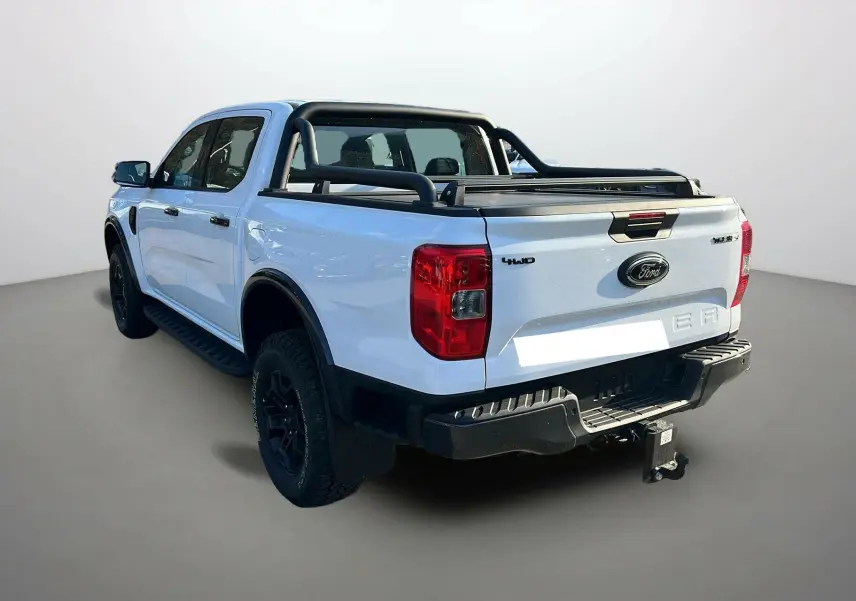 Ford Ranger blanc glacier en 3/4 arrière droit, avec arceaux noirs, attelage et benne couverte.
