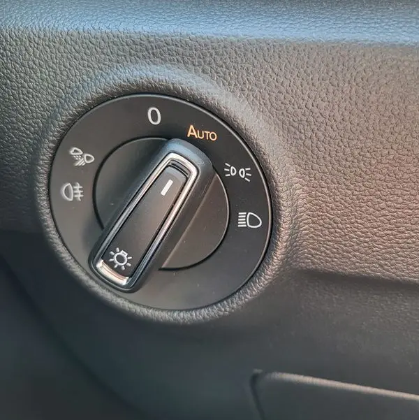 Gros plan sur le bouton de commande des phares du Volkswagen T-Roc gris Indium, avec réglage en mode automatique visible.