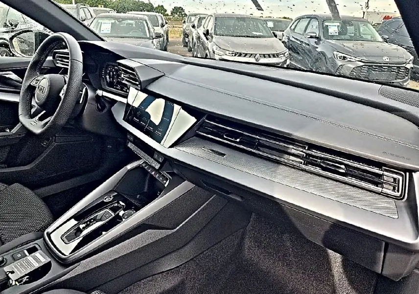 Vue intérieure côté conducteur de l'Audi A3 Sportback 2026 avec tableau de bord noir et écran tactile central.