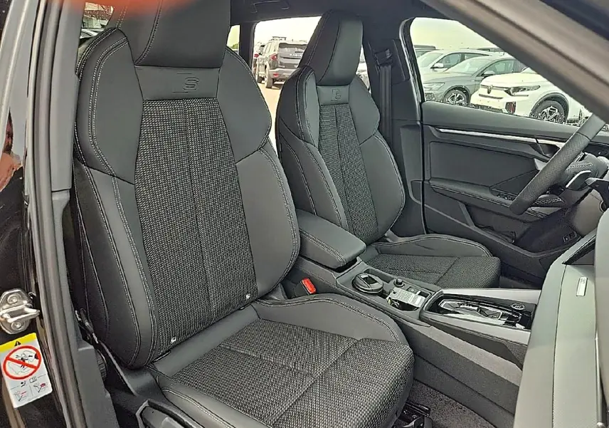 Vue intérieure avant de l'Audi A3 Sportback 2026 noir mythos, sièges sport S avec surpiqûres blanches et console centrale.