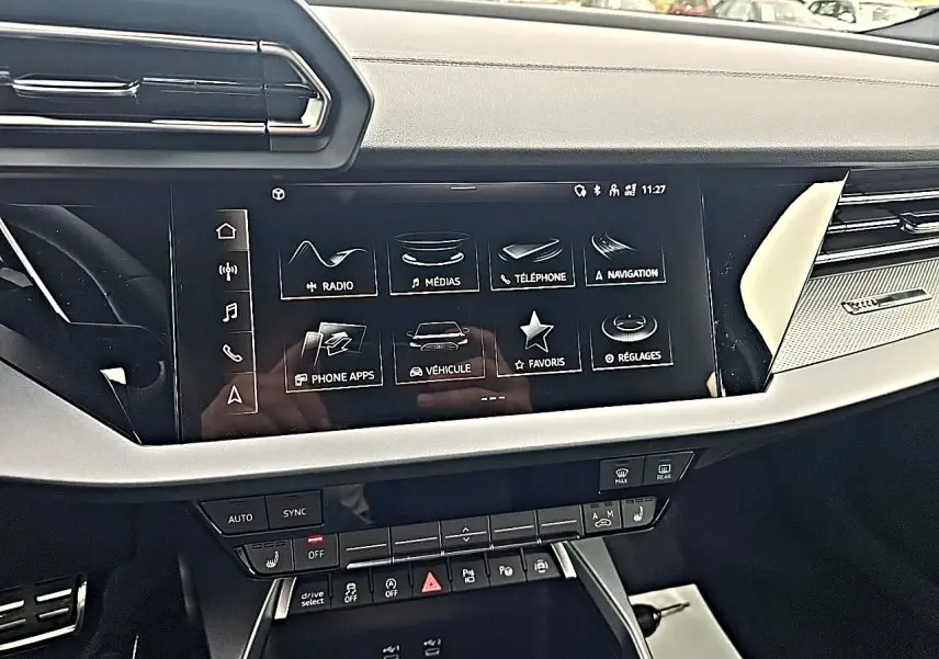 Vue intérieure du tableau de bord de l'Audi A3 Sportback 2026, écran tactile multifonction et commandes climatisation visibles.
