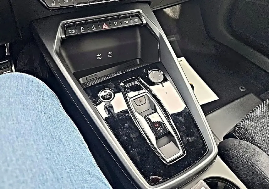 Vue rapprochée de la console centrale noire brillante de l'Audi A3 Sportback 2026 avec levier de vitesses automatique et boutons de contrôle.