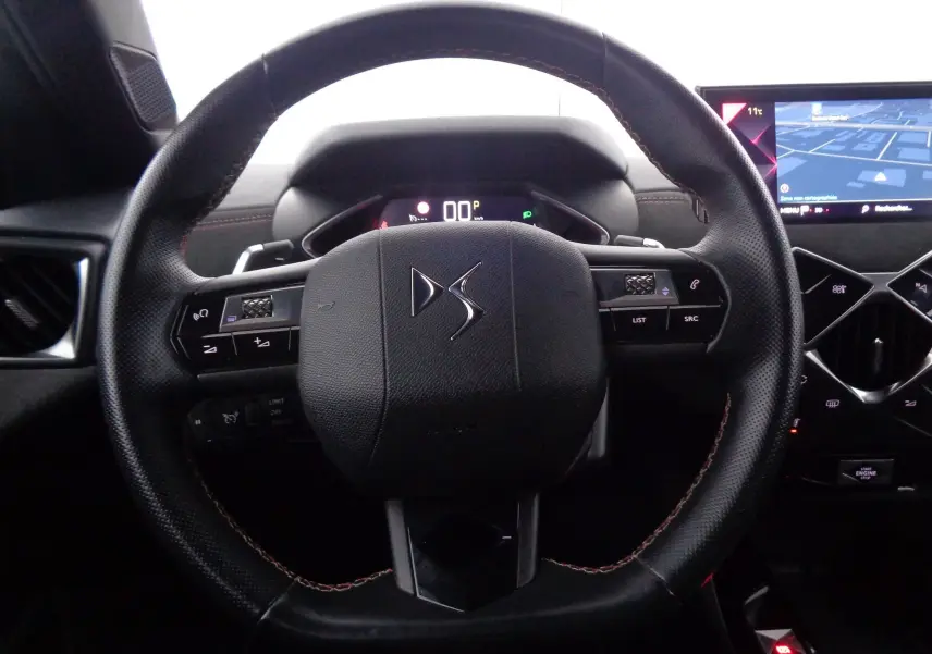 Volant en cuir noir avec logo DS au centre, tableau de bord numérique et écran tactile de navigation visible à droite.