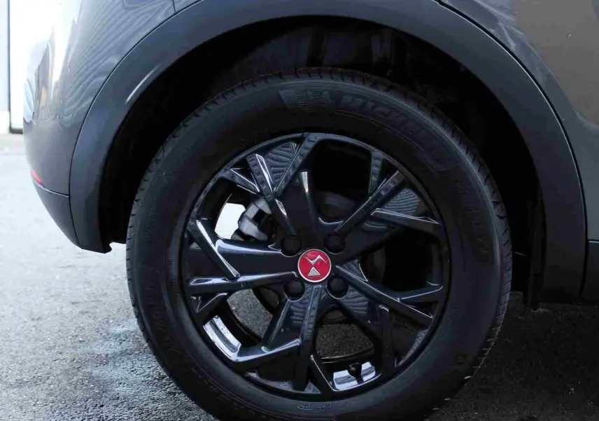 Gros plan sur la roue arrière droite du DS3 Crossback gris platinium métal, jante noire brillante avec logo rouge au centre.