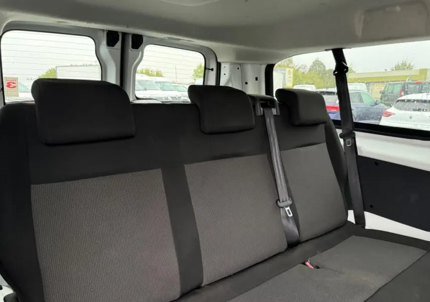 Vue intérieure sur la banquette arrière en tissu gris clair du Toyota Proace Fourgon blanc, avec ceinture et fenêtres latérales visibles.