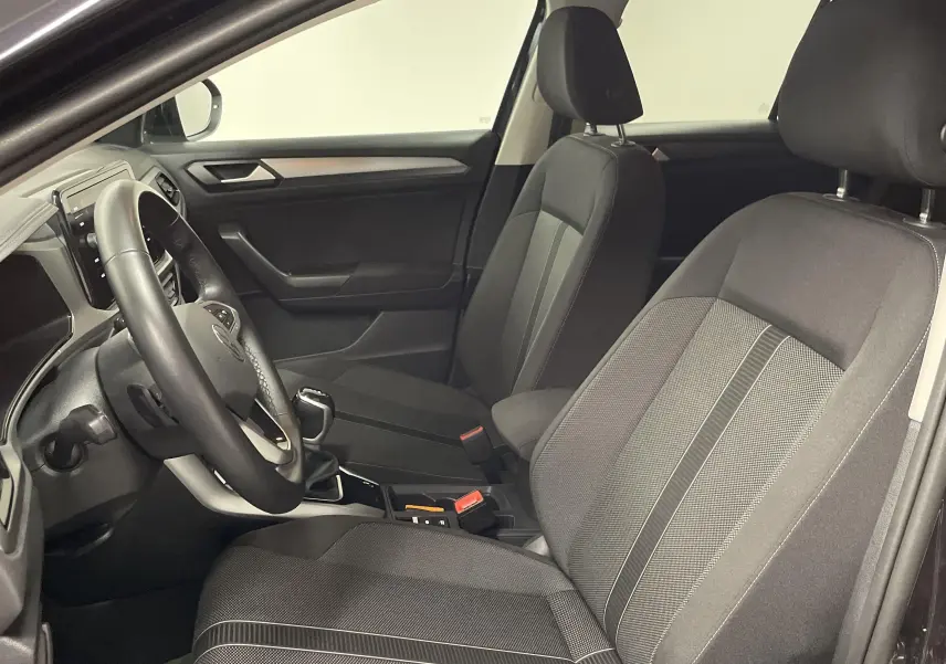 Intérieur côté conducteur du Volkswagen T-Roc 2024 noir, montrant sièges tissu et tableau de bord moderne.