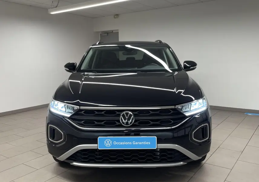 Vue frontale d'un Volkswagen T-Roc 1.5 TSI 150 DSG7 noir intense nacré avec phares LED allumés en intérieur.