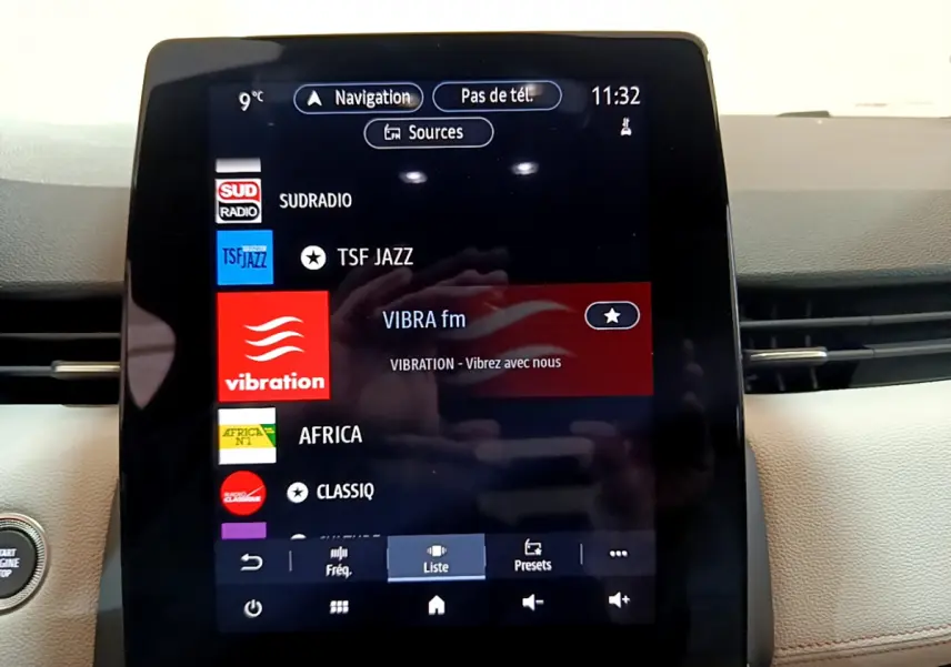 Écran tactile central affichant les stations radio dans l'habitacle clair de la Renault Clio Initiale Paris orange.