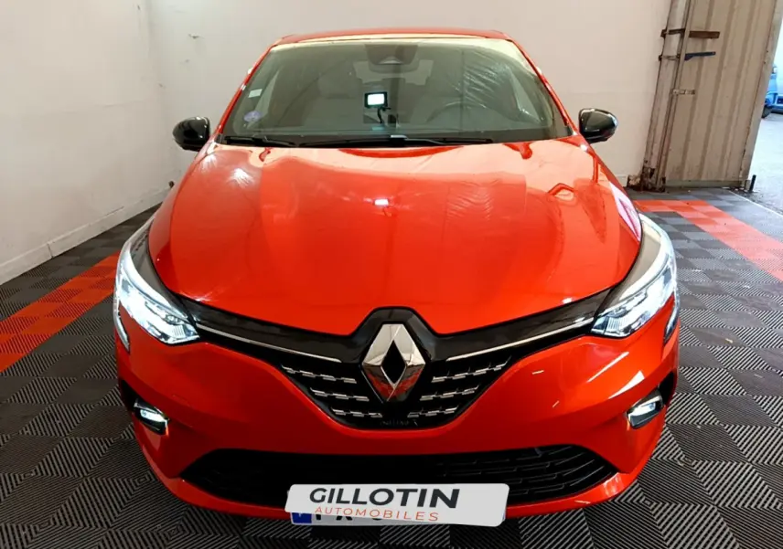 Vue avant d'une Renault Clio Initiale Paris E-TECH 140 orange avec phares LED allumés dans un garage.