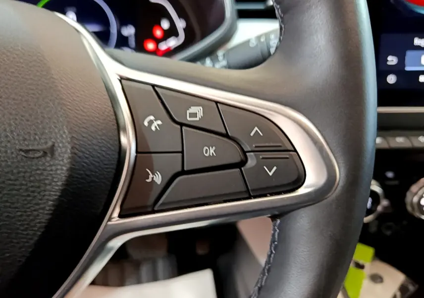 Gros plan sur les commandes du volant droit en cuir noir de la Renault Clio Initiale Paris orange, avec écran tactile en arrière-plan.