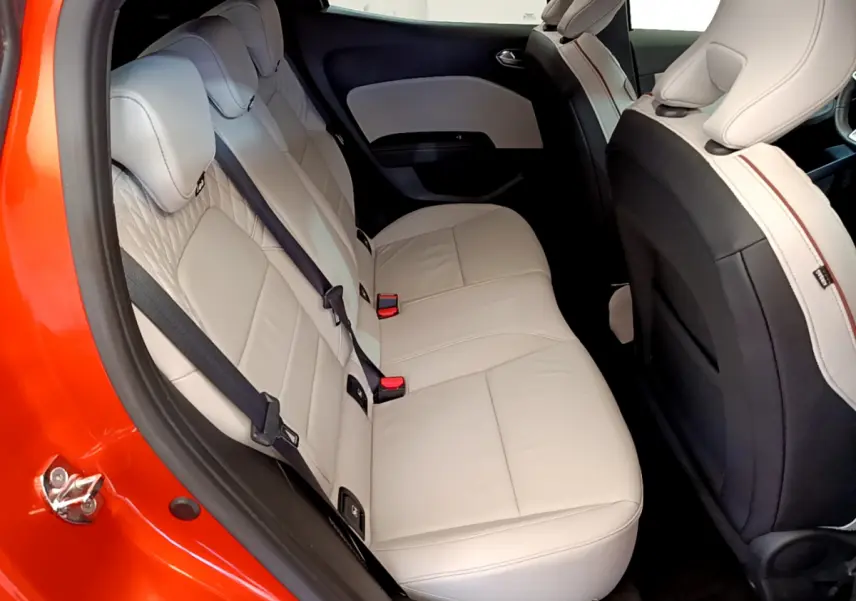 Vue intérieure arrière droite d'une Renault Clio orange avec sièges arrière en cuir beige clair et ceintures noires.