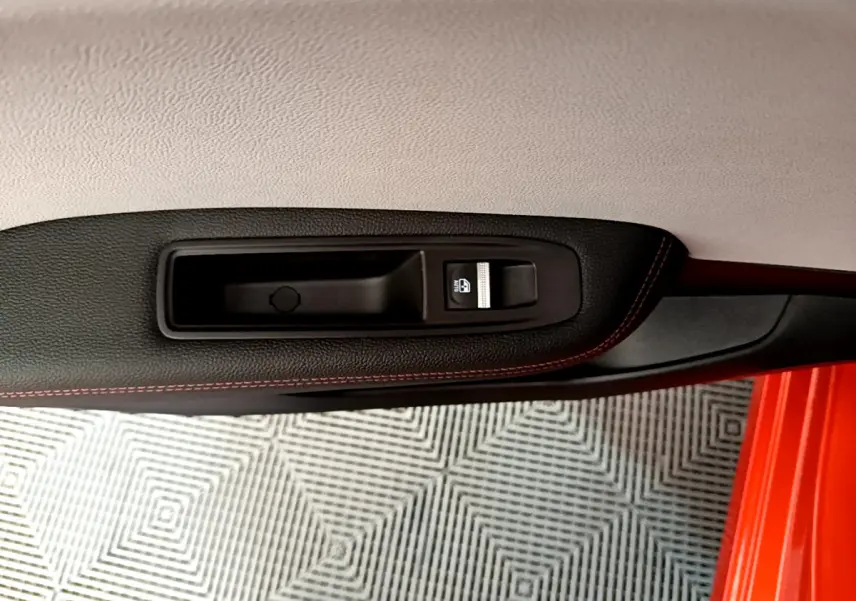 Gros plan sur la poignée intérieure et bouton de verrouillage de porte côté gauche d'une Renault Clio orange 2021.